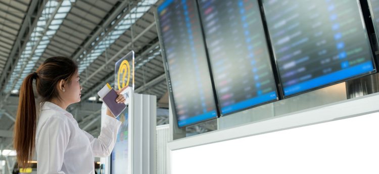 Asian young woman in international airport looking at the flight information board, checking her flight in airport.