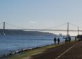 Portuguese Golden Visa Requirements: 2025 Investment & Compliance Rules — Scenic view of a suspension bridge over a calm river with people walking along the riverside path.