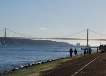 Portuguese Golden Visa Requirements: 2025 Investment & Compliance Rules — Scenic view of a suspension bridge over a calm river with people walking along the riverside path.