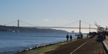 Portuguese Golden Visa Requirements: 2025 Investment & Compliance Rules — Scenic view of a suspension bridge over a calm river with people walking along the riverside path.