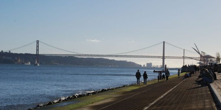 Portuguese Golden Visa Requirements: 2025 Investment & Compliance Rules — Scenic view of a suspension bridge over a calm river with people walking along the riverside path.