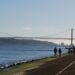 Portuguese Golden Visa Requirements: 2025 Investment & Compliance Rules — Scenic view of a suspension bridge over a calm river with people walking along the riverside path.